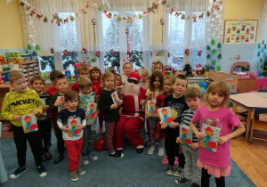 Zdjęcie grupowe z Mikołajem, dzieci prezentują otrzymane książeczki.